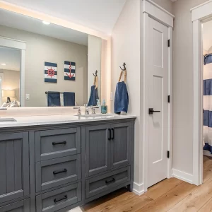 Nautical bathroom with gray double vanity, lighted mirror, anchor shower curtain, wood flooring, and black hardware