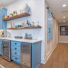 Built-in blue beverage bar with open wood shelves, wine refrigerator, undercounter beverage cooler, and hallway access
