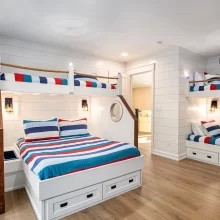 Custom bunk room with built-in beds, striped bedding, rope railings, porthole-style details, shiplap walls, and wood flooring