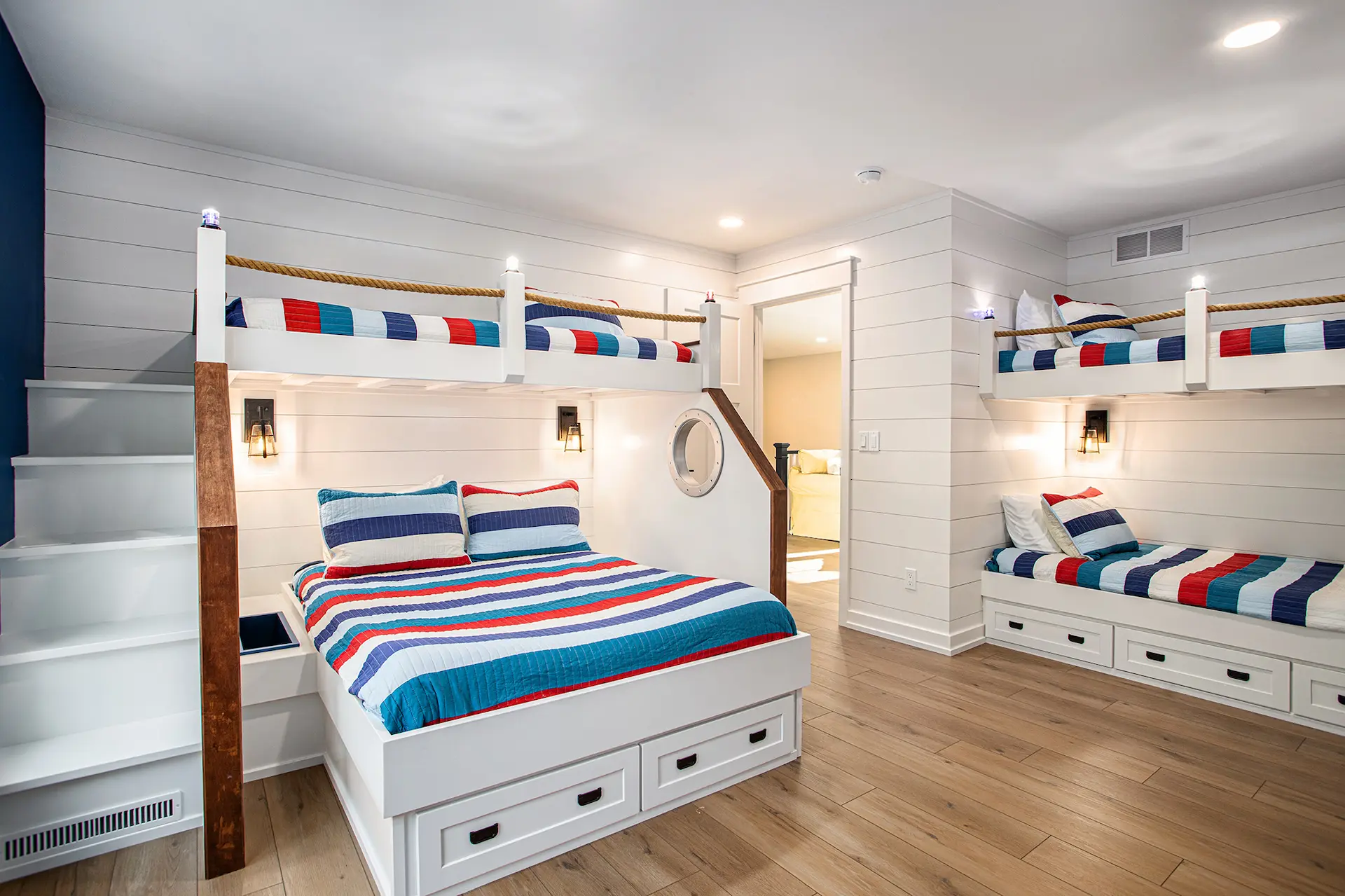 Custom bunk room with built-in beds, striped bedding, rope railings, porthole-style details, shiplap walls, and wood flooring