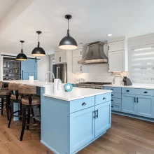 Blue custom kitchen with large island, white counters, stainless range hood, and lake-facing windows