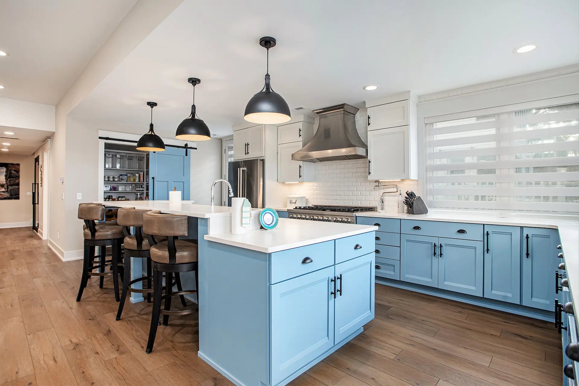 Blue custom kitchen with large island, white counters, stainless range hood, and lake-facing windows
