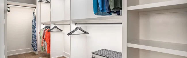 Custom Walk-In Closet with Hanging Storage | Pennings & Sons Walk-in closet with custom white shelving, hanging rods, accent lighting, and wood flooring