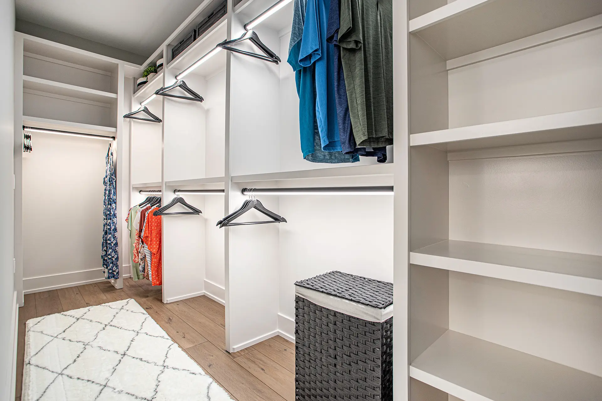 Walk-in closet with custom white shelving, hanging rods, accent lighting, and wood flooring