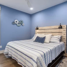 Blue bedroom with striped bedding, wood-look headboard, wall sconces, and decorative wall art