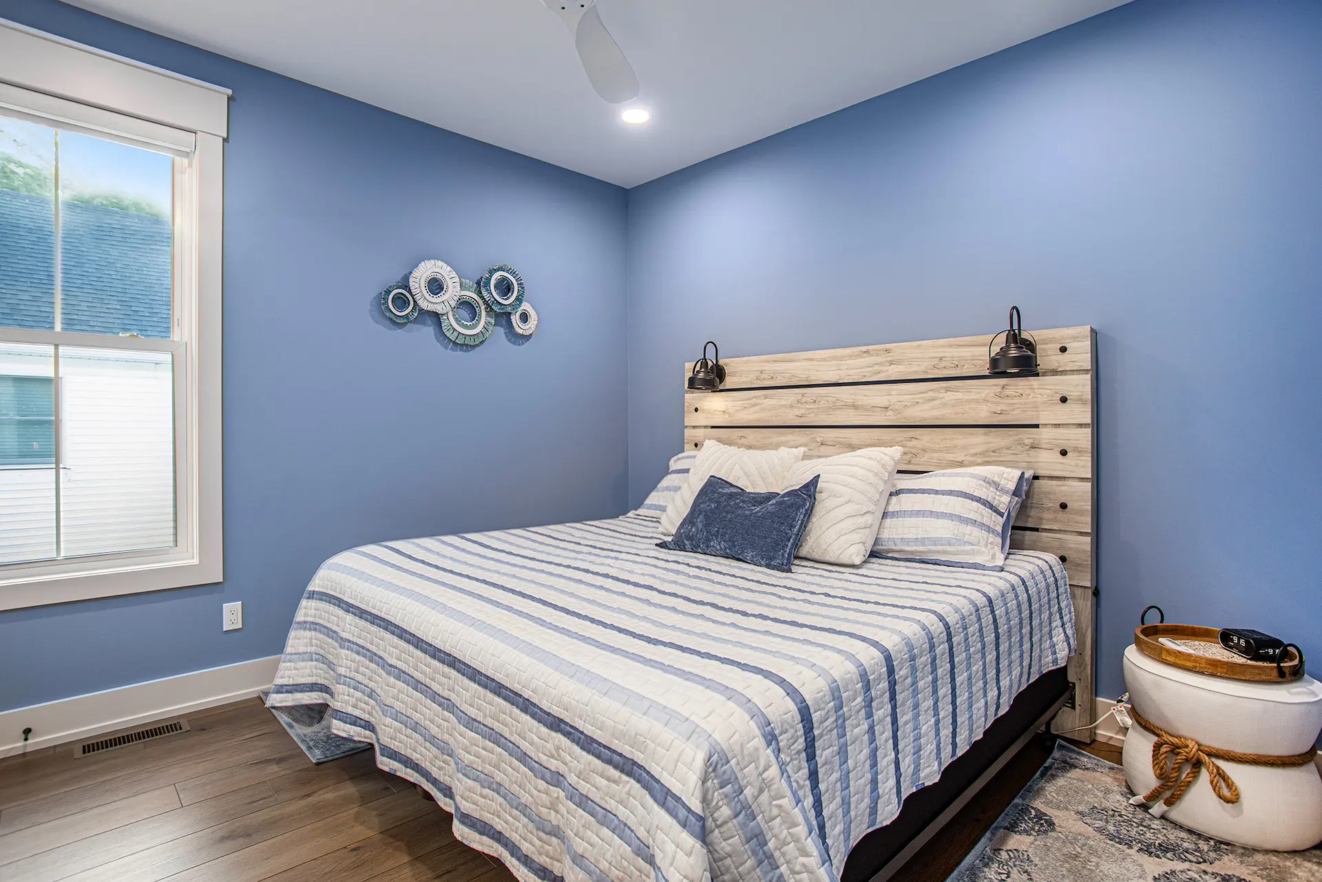 Blue bedroom with striped bedding, wood-look headboard, wall sconces, and decorative wall art