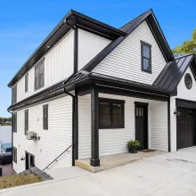Angled exterior view of modern lakefront home with black trim, covered entry, black garage door, white siding, concrete driveway, and lake view