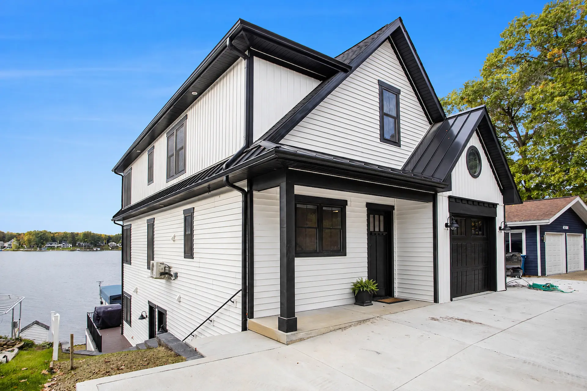 Angled exterior view of modern lakefront home with black trim, covered entry, black garage door, white siding, concrete driveway, and lake view