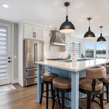 Blue kitchen island with white countertop, barstools, stainless appliances, black pendant lights, and lake view