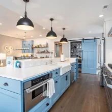 Spacious blue kitchen with island sink, stainless appliances, black pendant lighting, and walk-in pantry with blue barn door