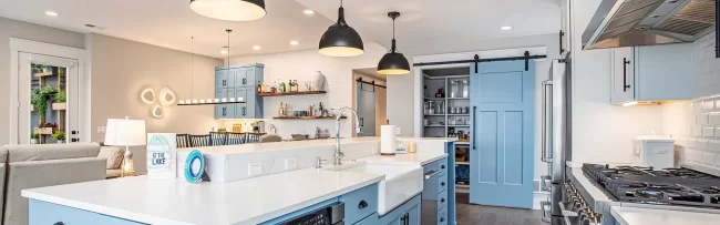 Spacious blue kitchen with island sink, stainless appliances, black pendant lighting, and walk-in pantry with blue barn door