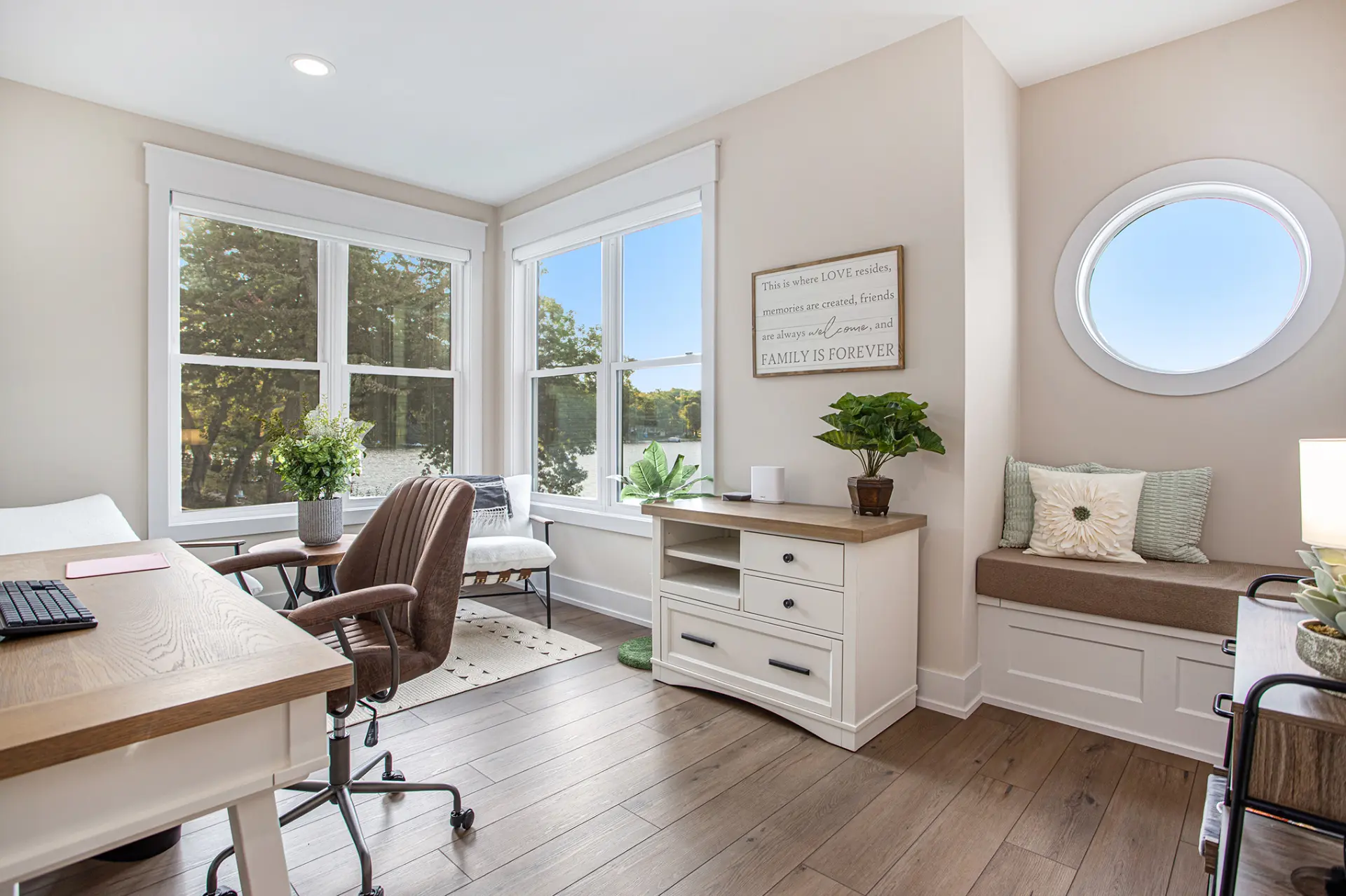 Bright home office with lake views, desk, sitting area, window seat, round window, and built-in storage