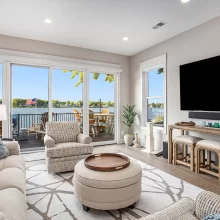 Lakefront living room with large sliding glass doors, beige seating, wall-mounted TV, and deck with lake view
