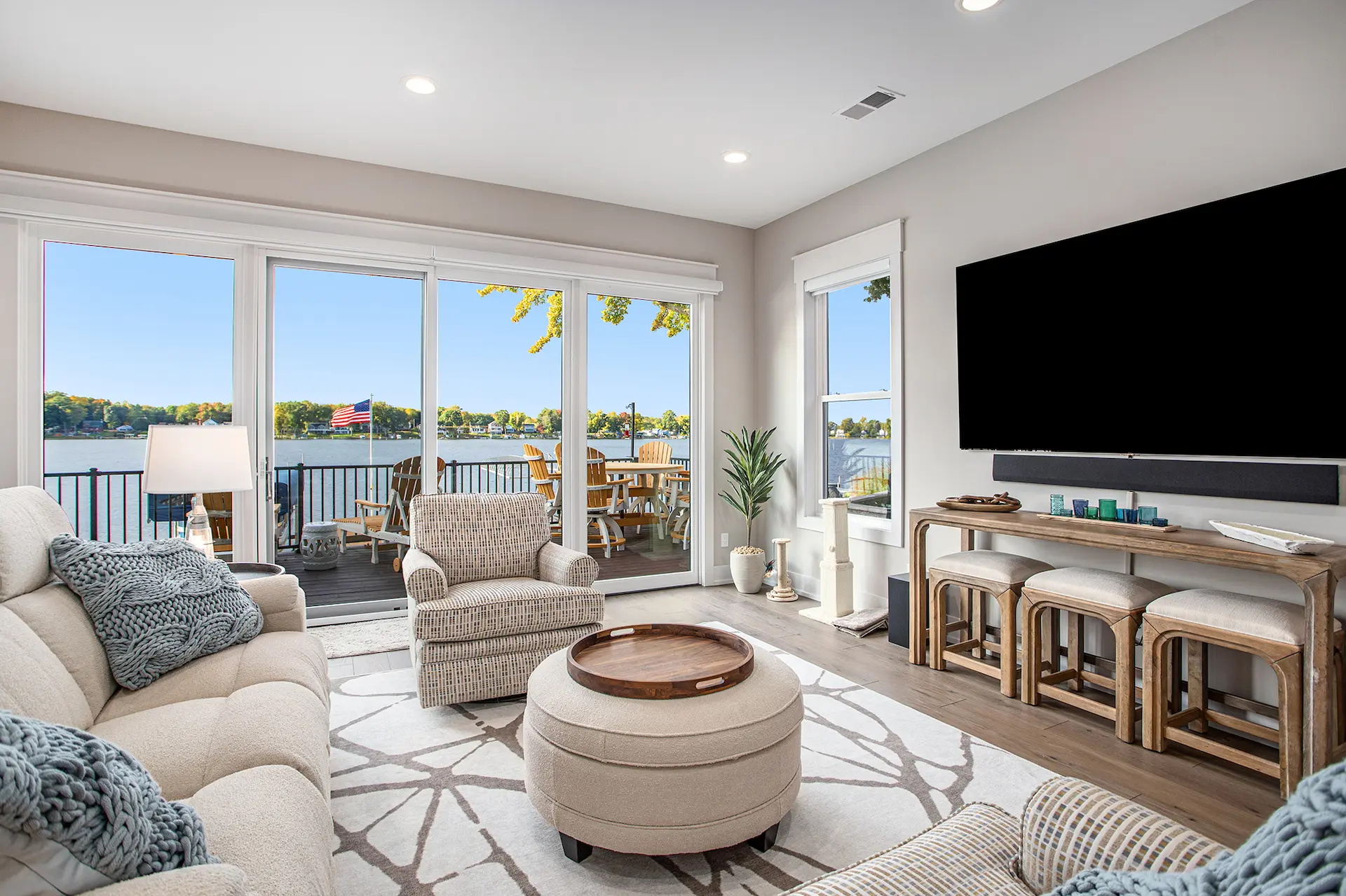 Lakefront living room with large sliding glass doors, beige seating, wall-mounted TV, and deck with lake view