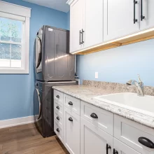 Laundry room with stacked washer and dryer, white cabinets, granite countertop, utility sink, and blue walls