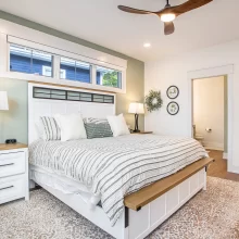 Primary bedroom with white bed, green accent wall, ceiling fan, nightstands, and ensuite bathroom access