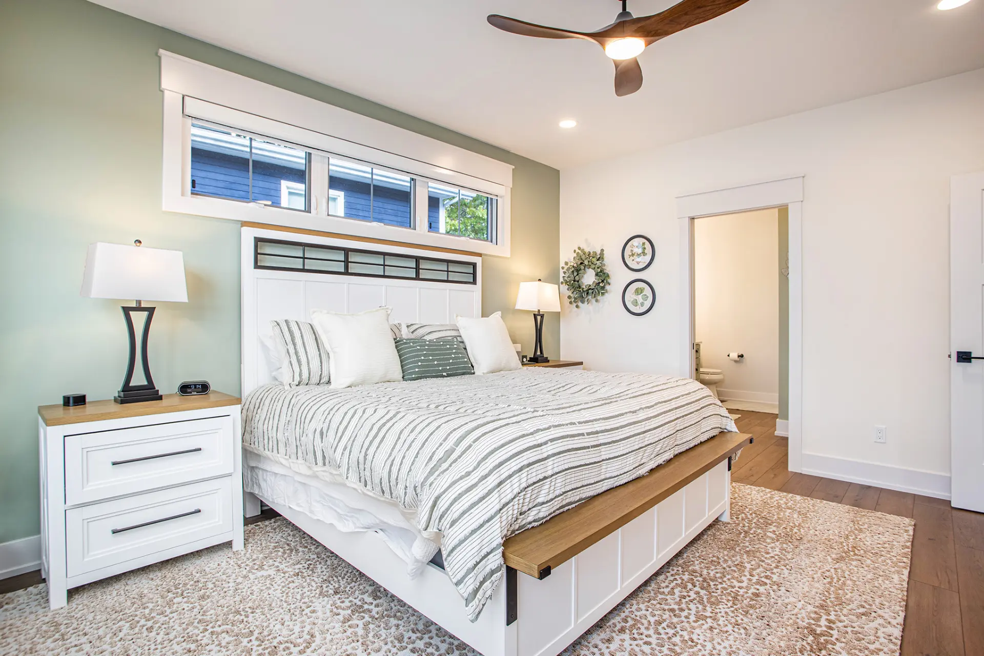 Primary bedroom with white bed, green accent wall, ceiling fan, nightstands, and ensuite bathroom access