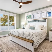 Primary bedroom with green accent wall, white bed frame, transom windows, lake views, and ceiling fan