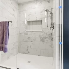 Walk-in shower with marble-look wall tile, white penny tile floor, glass enclosure, and polished fixtures in a downtown Kalamazoo condominium