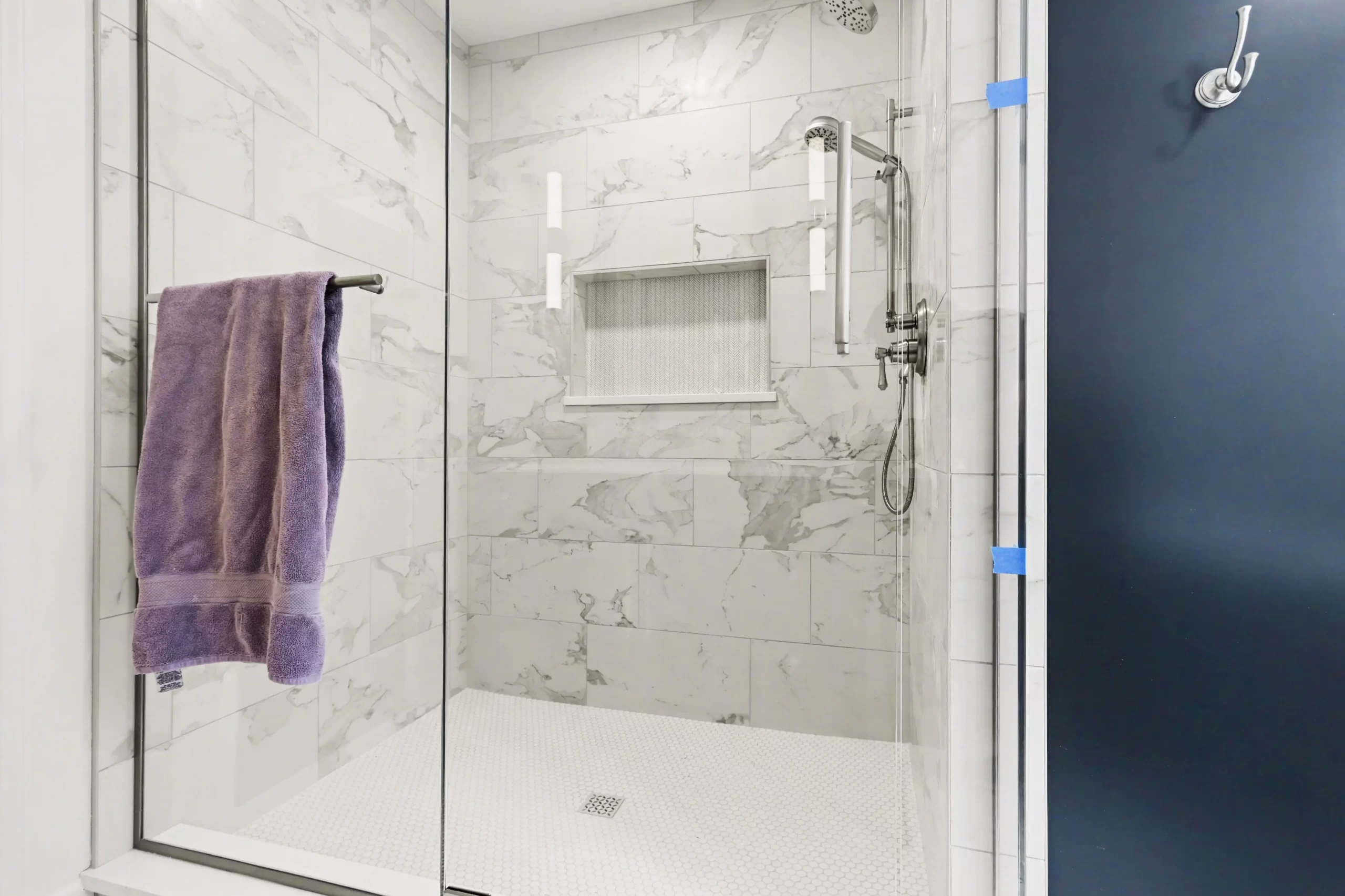 Walk-in shower with marble-look wall tile, white penny tile floor, glass enclosure, and polished fixtures in a downtown Kalamazoo condominium