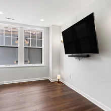 Small media room with wall-mounted TV, dark wood flooring, modern sconces, and two divided-light windows in a downtown Kalamazoo condominium