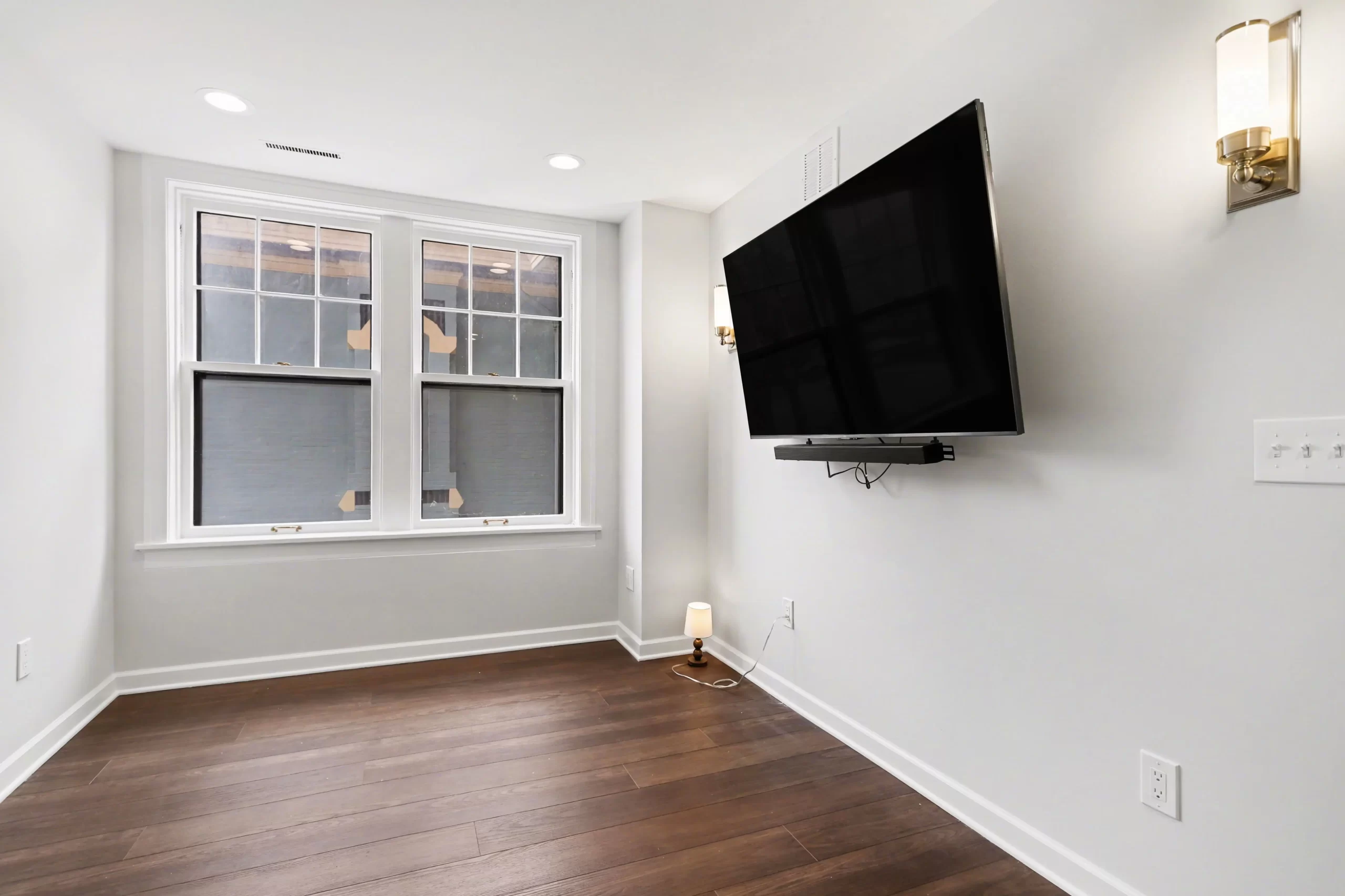 Small media room with wall-mounted TV, dark wood flooring, modern sconces, and two divided-light windows in a downtown Kalamazoo condominium