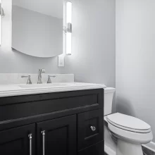 Compact powder bathroom with black vanity, marble-look countertop, toilet, and modern vertical sconces in a downtown Kalamazoo condominium