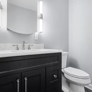 Compact powder bathroom with black vanity, marble-look countertop, toilet, and modern vertical sconces in a downtown Kalamazoo condominium