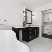 Wide primary bathroom view with clawfoot tub, black vanity, glass shower, white tile floor, and adjacent closet cabinetry in a downtown Kalamazoo condominium