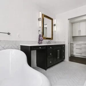 Wide primary bathroom view with clawfoot tub, black vanity, glass shower, white tile floor, and adjacent closet cabinetry in a downtown Kalamazoo condominium