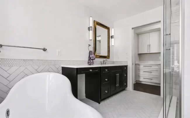 Primary Bath with Tub, Vanity, and Shower | Pennings & Sons Wide primary bathroom view with clawfoot tub, black vanity, glass shower, white tile floor, and adjacent closet cabinetry in a downtown Kalamazoo condominium