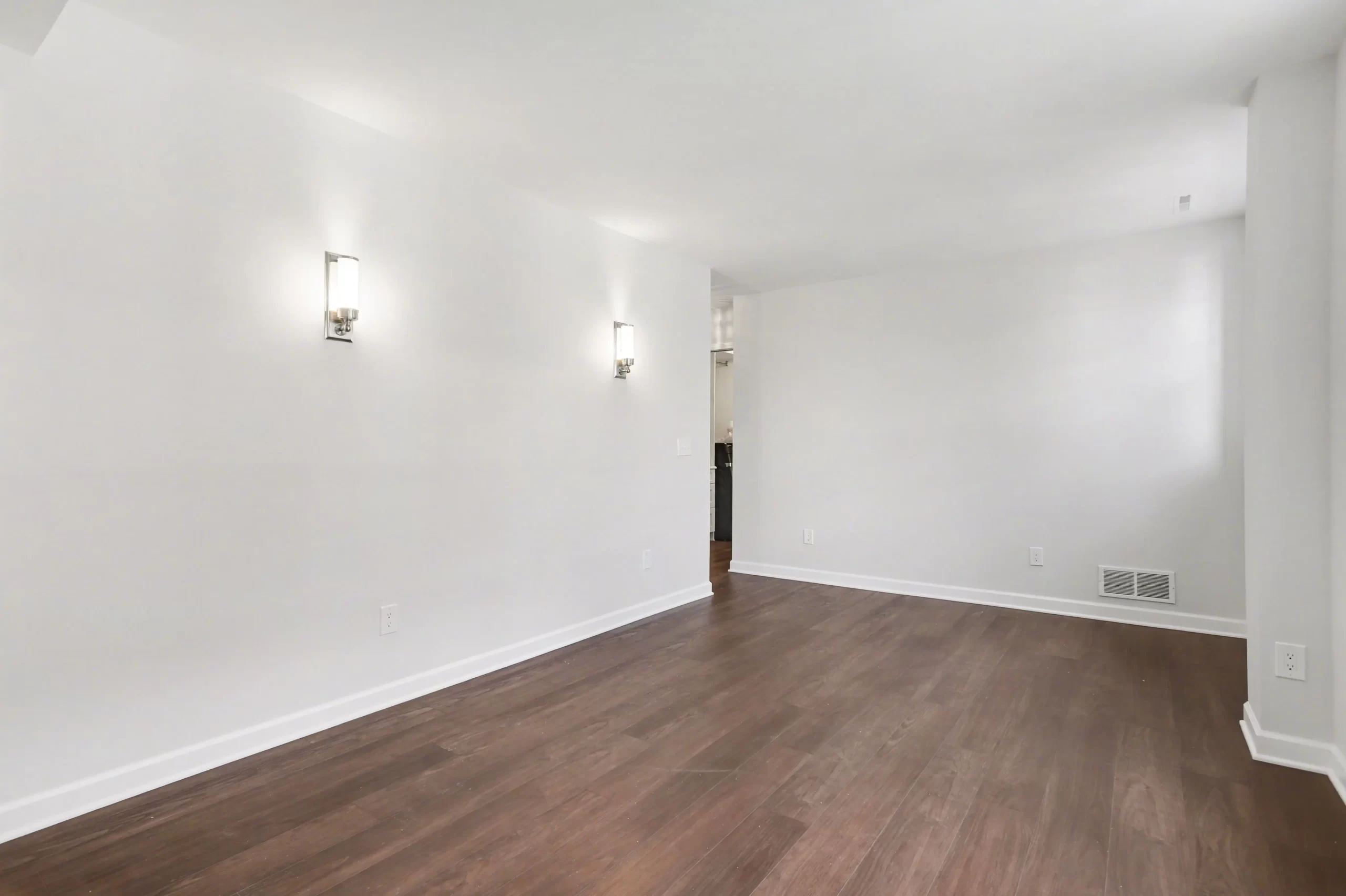 Unfurnished flex room with dark wood flooring, neutral walls, white trim, and modern wall sconces in a downtown Kalamazoo condominium