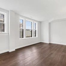 Unfurnished room with dark hardwood flooring, white trim, wall sconces, and large windows in a downtown Kalamazoo condominium