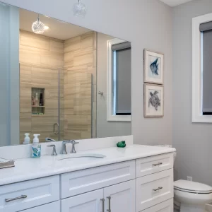 Bathroom with white vanity, large wall mirror, chrome fixtures, gray walls, and wood-look tile shower visible in the reflection