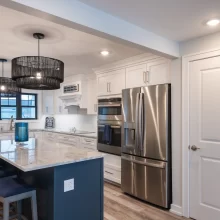White kitchen with blue island, marble-look countertops, stainless appliances, and woven pendant lights