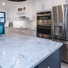 Kitchen detail showing marble-look island countertop, stainless refrigerator, double wall oven, and white cabinetry