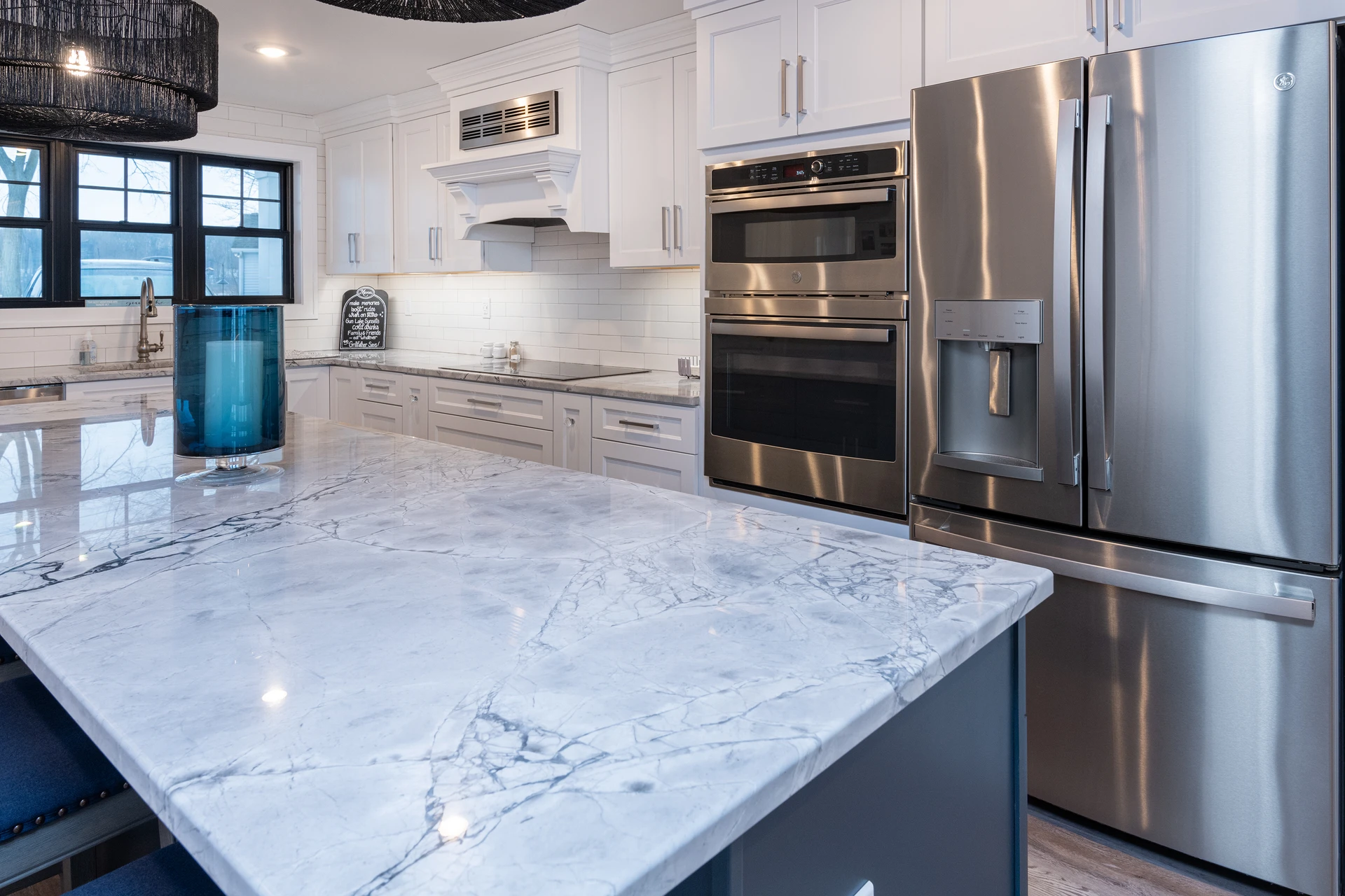 Kitchen detail showing marble-look island countertop, stainless refrigerator, double wall oven, and white cabinetry