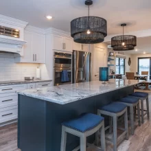 Open kitchen with blue island, white cabinetry, marble-look countertops, bar stools, and lakefront living area beyond