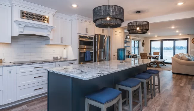 Blue Island Kitchen with Open Living View | Pennings & Sons Open kitchen with blue island, white cabinetry, marble-look countertops, bar stools, and lakefront living area beyond