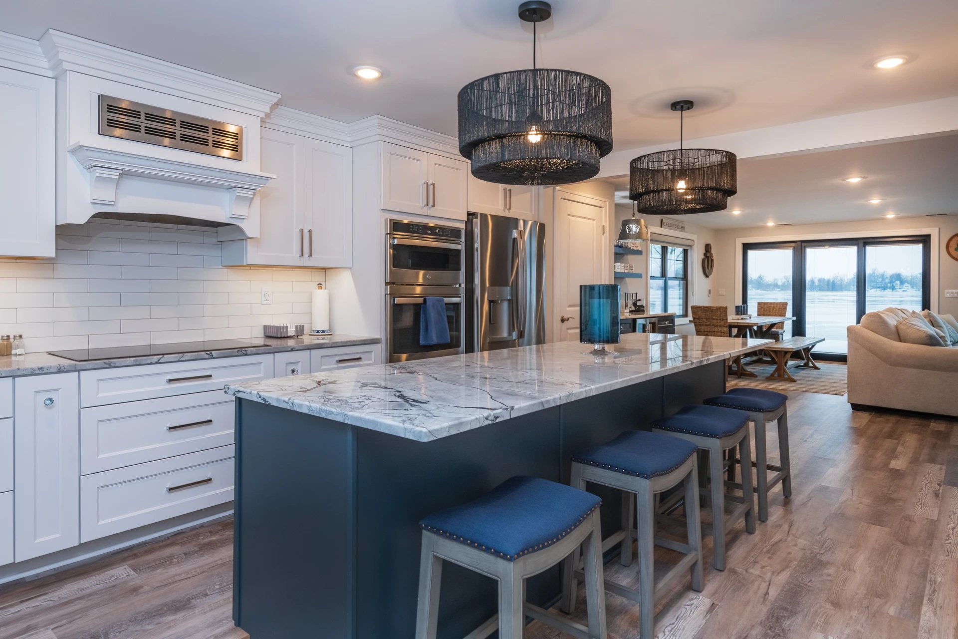 Open kitchen with blue island, white cabinetry, marble-look countertops, bar stools, and lakefront living area beyond