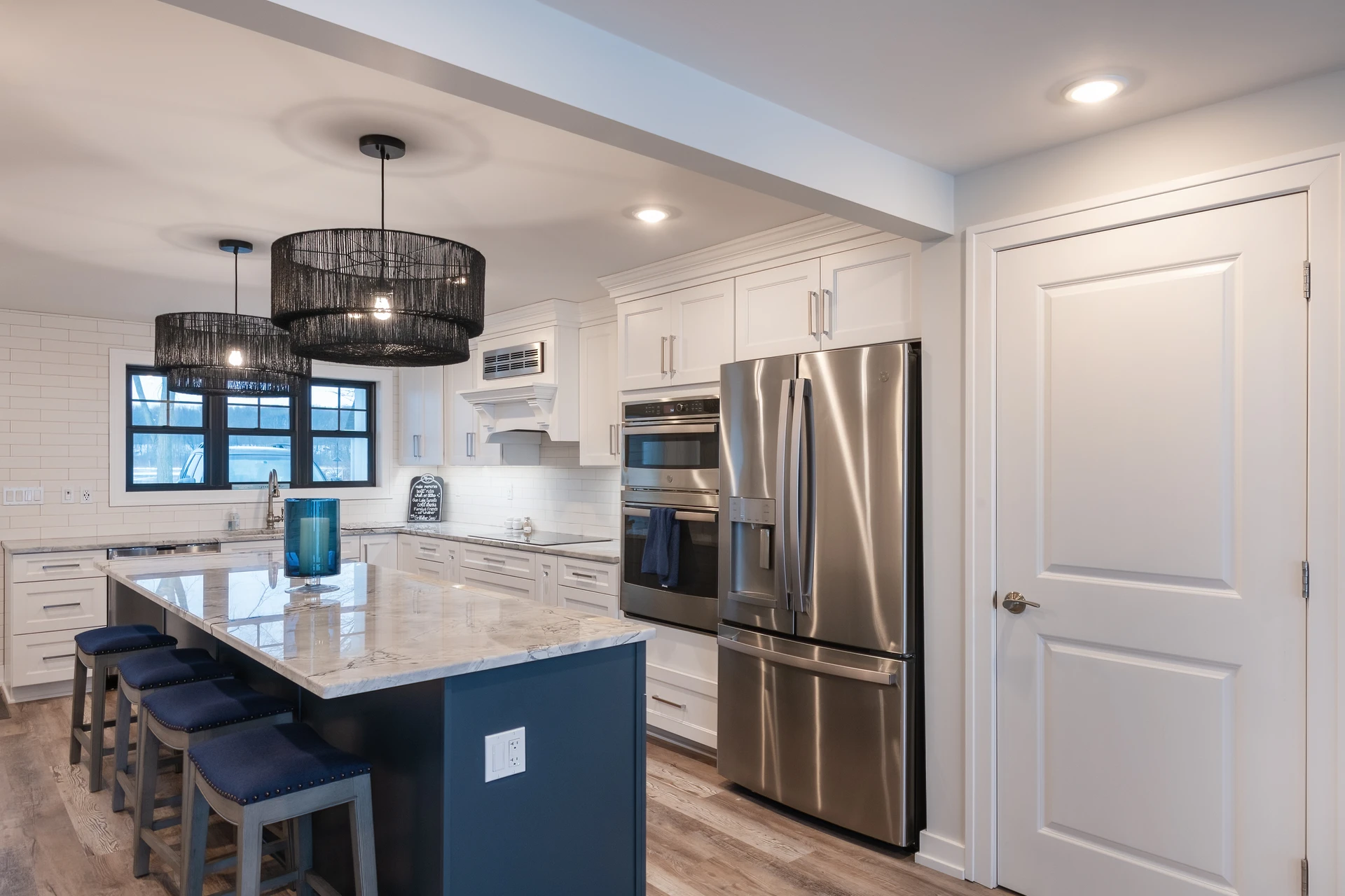 White kitchen with blue island, marble-look countertops, stainless appliances, and woven pendant lights