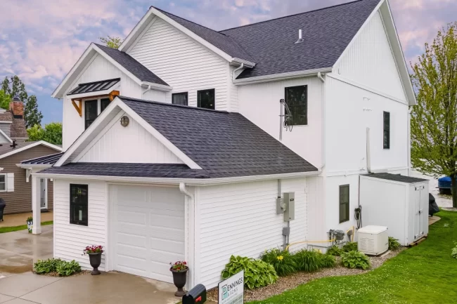 Lakefront Home Garage and Side Exterior | Pennings & Sons Side exterior of white lakefront home with attached garage, dark shingle roof, landscaped foundation, and lake visible beyond