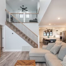 Bright open living room with staircase, black balusters, kitchen island, and gray wood-look flooring