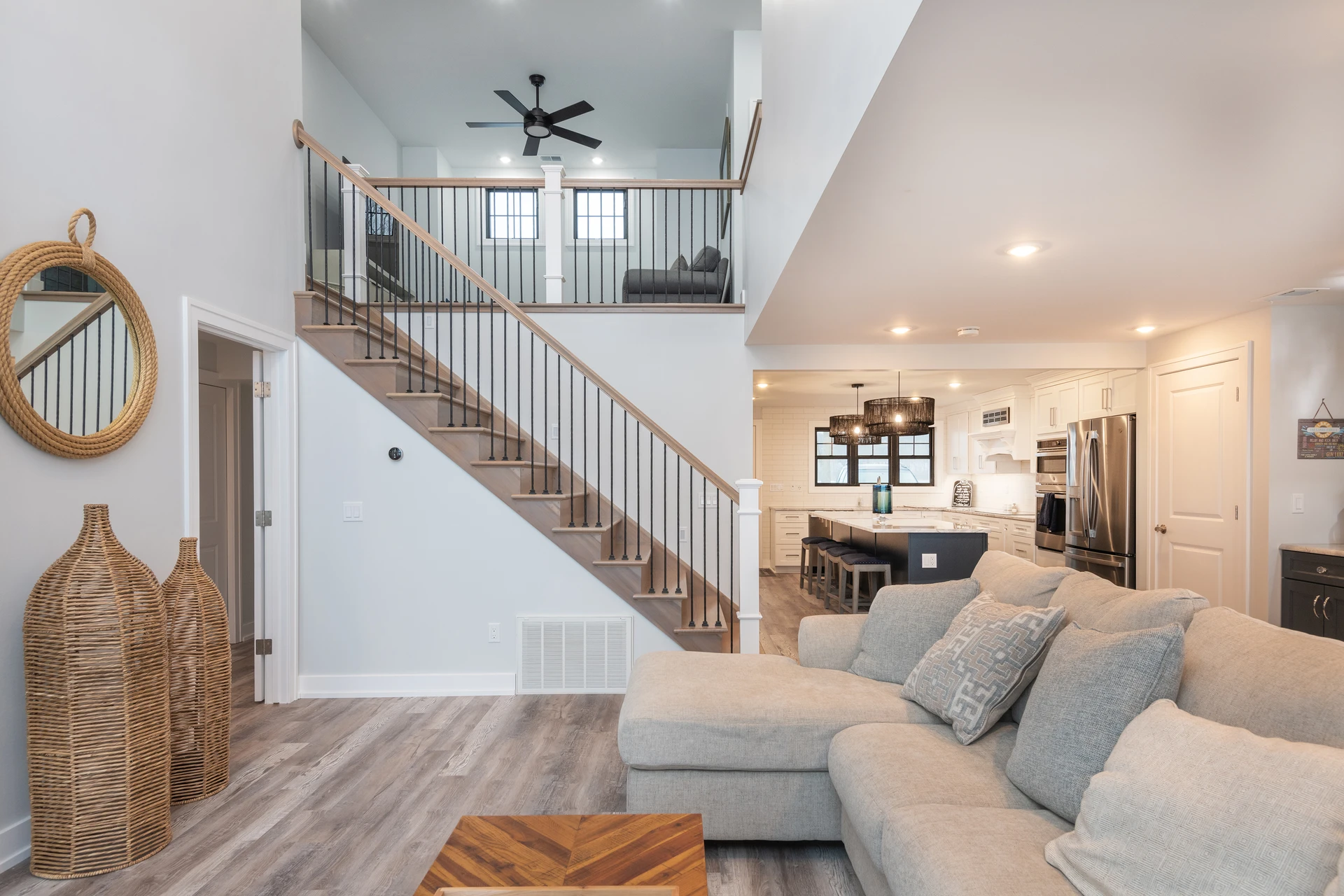 Bright open living room with staircase, black balusters, kitchen island, and gray wood-look flooring