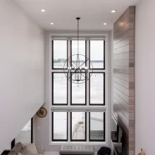 Overhead view of two-story living room with large lake-facing window, chandelier, and tall wood fireplace wall