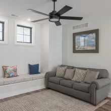 Loft Sitting room with gray sofa, built-in window bench, black-framed windows, ceiling fan, and coastal wall art