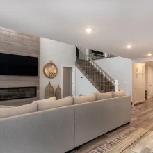 Open living room with gray wood-look flooring, shiplap-style fireplace wall, staircase, and kitchen beyond