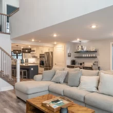 Open living space with sectional seating, custom staircase, kitchen island, wet bar, and lake-facing windows