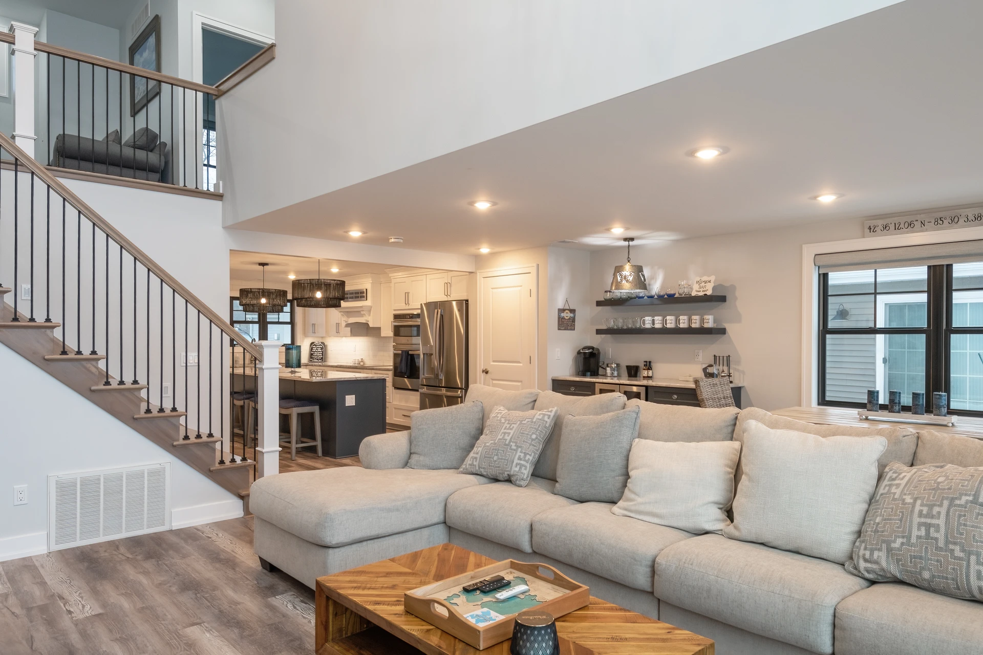 Open living space with sectional seating, custom staircase, kitchen island, wet bar, and lake-facing windows
