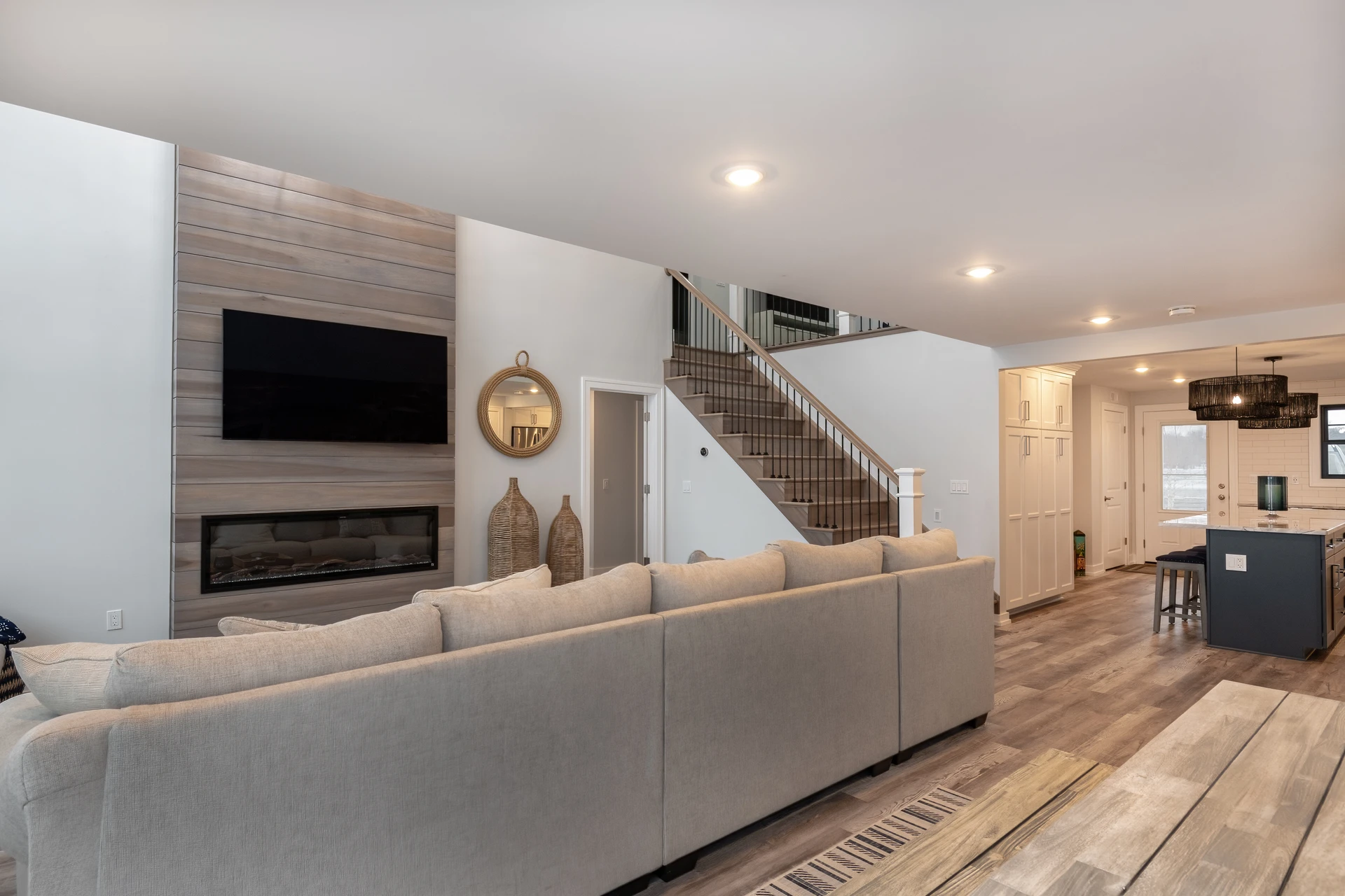 Open living room with gray wood-look flooring, shiplap-style fireplace wall, staircase, and kitchen beyond